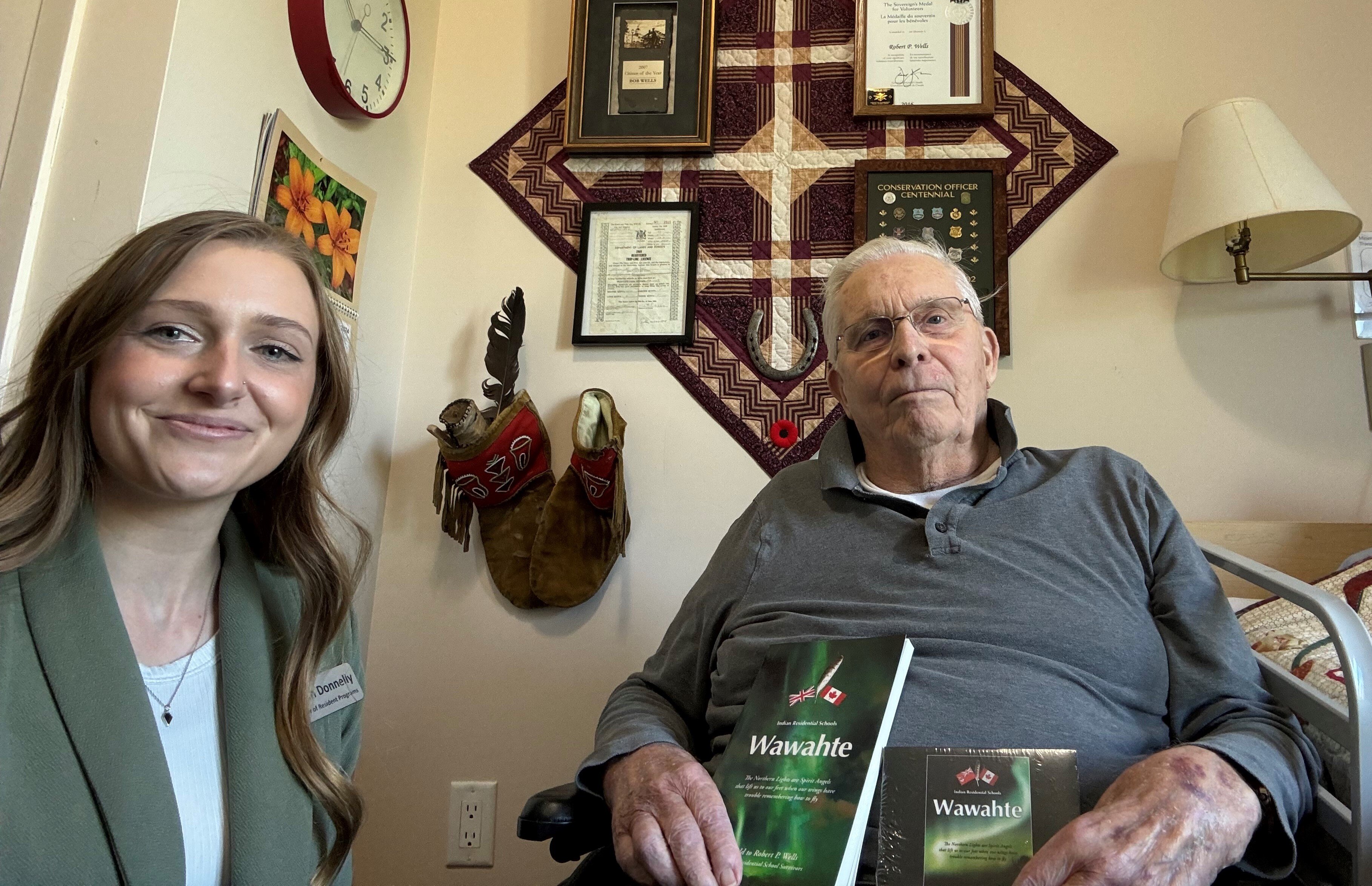 Bob Wells, a resident at Granite Ridge Community sitting beside Kyarah Donnelly Director of Resident Programs, is holding two books he authored 